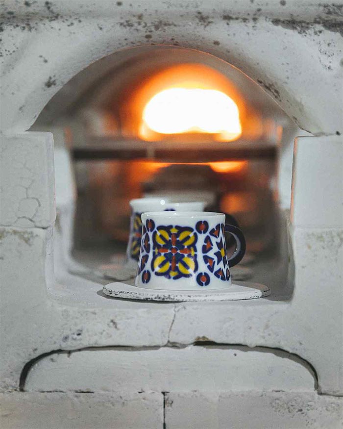 Two ceramic mugs with colorful patterns inside a lit fireplace.